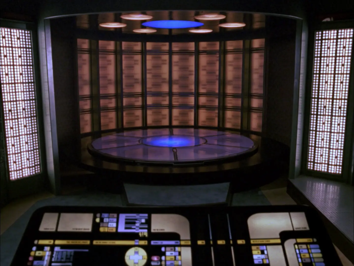 A futuristic transporter room from a starship, featuring a circular transport pad with glowing blue lights and a surrounding control console displaying LCARS interface. The walls are lined with illuminated panels, and overhead lights highlight the center of the pad.